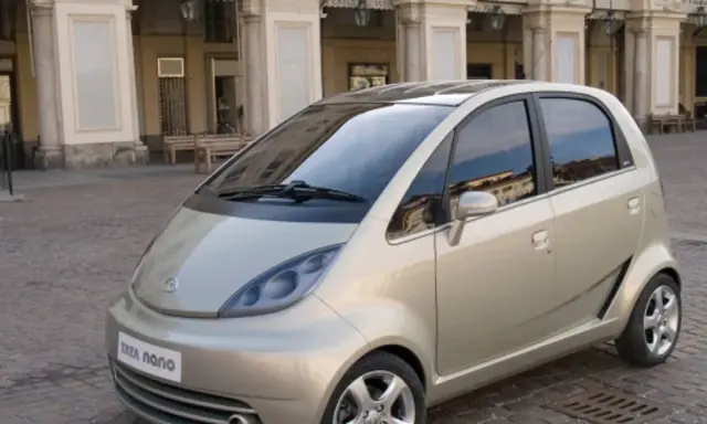 Złoty Tata Nano na brukowanym placu przed zabytkową kamienicą.