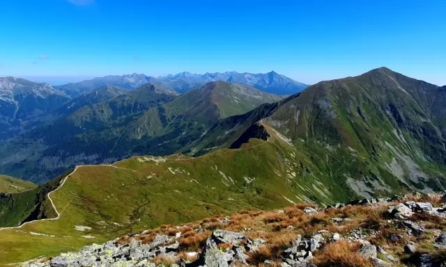 Widok na pasmo górskie z wyraźną ścieżką wijącą się po zboczu. W oddali widać kolejne szczyty Tatr, w tym Starorobociański Wierch.