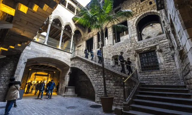 Gente paseando por un patio interior con palmera, escaleras de piedra y arcos. Ideal para visitar museos gratis domingo Barcelona.