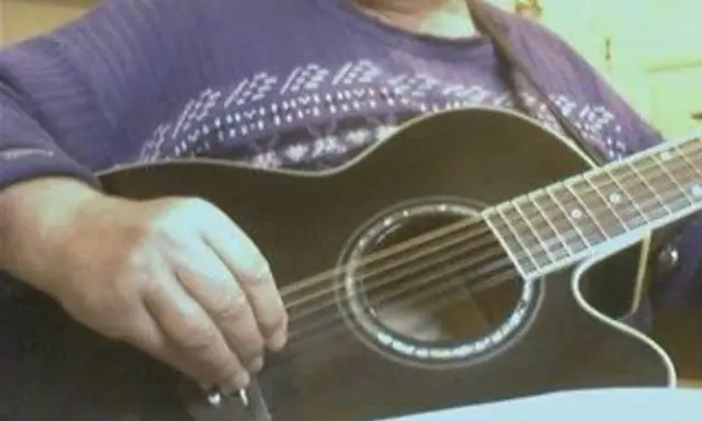Main d'un musicien ajustant l'accordage 12 cordes d'une guitare acoustique noire.