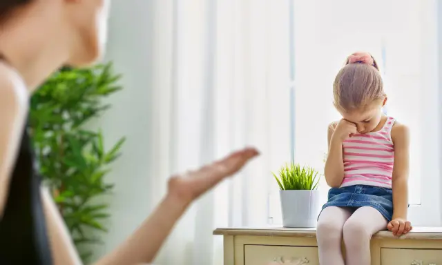 Smutna dziewczynka siedzi przy oknie, a jej mama gestykuluje. Warto nauczyć się, jak przestać krzyczeć na dziecko, by budować lepsze relacje.