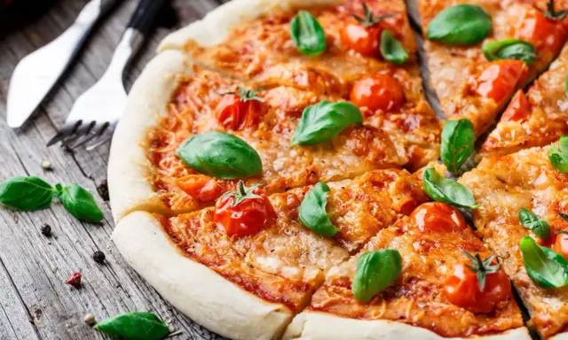Pyszna pizza Margherita, klasyka włoskiego jedzenia, z pomidorkami koktajlowymi i bazylią na drewnianym blacie.