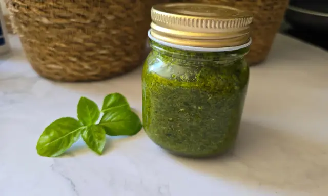 Un pot de pesto maison, vert vif, à côté de feuilles de basilic frais. Parfait pour sublimer vos plats !