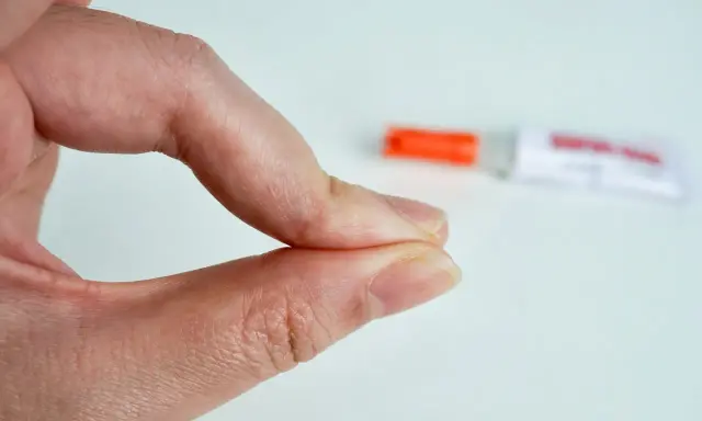 Fingerkuppen kleben zusammen. Ein Röhrchen mit debonder liegt unscharf im Hintergrund.