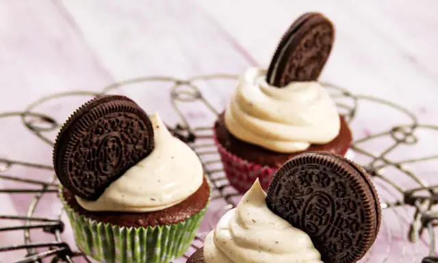 Drei leckere Oreo Muffins mit cremiger Glasur und einem ganzen Oreo-Keks darauf, auf einem Gitter.