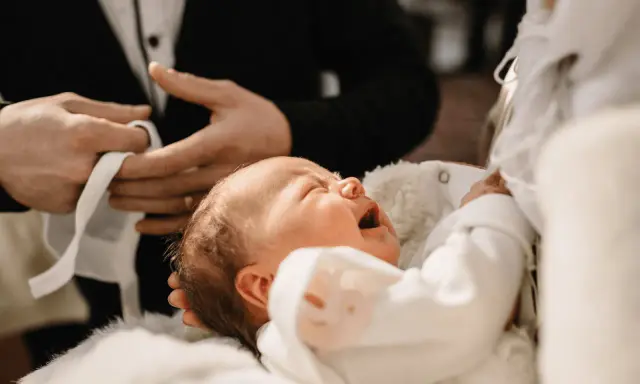 Płacz dziecka podczas chrztu krok po kroku. Dziecko w białej szatce, trzymane przez rodziców.