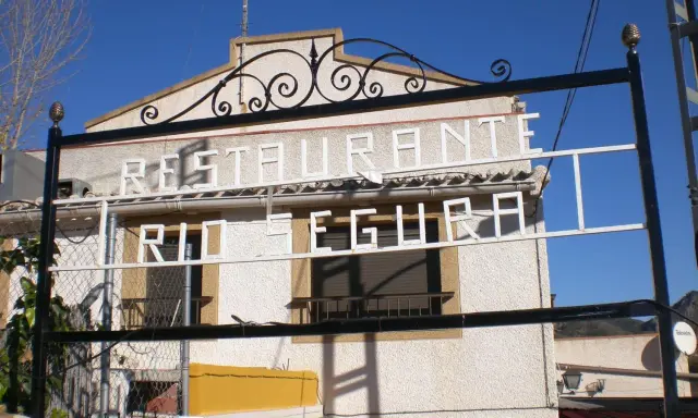 Restaurante El Gallego Elche de la Sierra, con letrero "Restaurante Río Segura" en blanco sobre fachada texturizada.