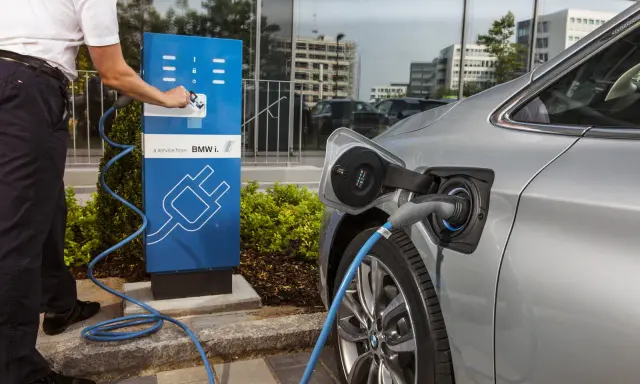 Un uomo collega un'auto elettrica a una colonnina di ricarica BMW i. Un passo verso il calcolo risparmio auto elettrica.
