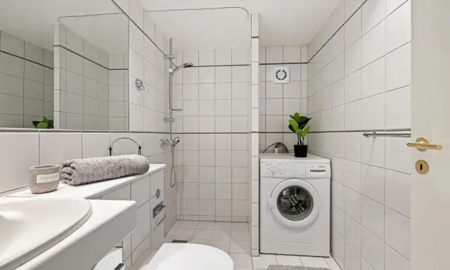 Baño con lavadora, ducha y un extractor de aire en la habitación para mantener la frescura.