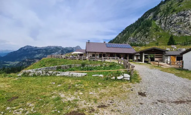 Malga Tuglia, un rifugio alpino con pannelli solari, immerso nel verde con montagne sullo sfondo.