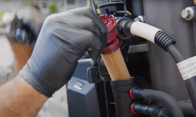Main d'un mécanicien en gant noir retirant un filtre à gasoil encrassé, conséquence d'un mauvais entretien.