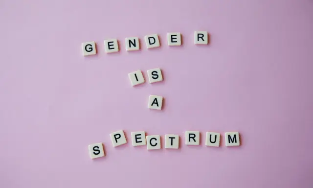 Litery układają napis "GENDER IS A SPECTRUM", podkreślając, że dysforia i niezgodność płciowa są częścią szerokiego spektrum tożsamości.