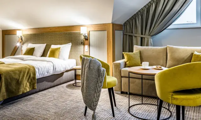 Przytulny pokój hotelowy z dwoma łóżkami, kanapą i fotelami. Idealne miejsce na relaks po podróży.
