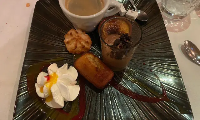 Un assortiment gourmand : café, financier, macaron, verrine chocolat et chantilly, servi sur une assiette noire texturée, digne de la taverne des fougères.