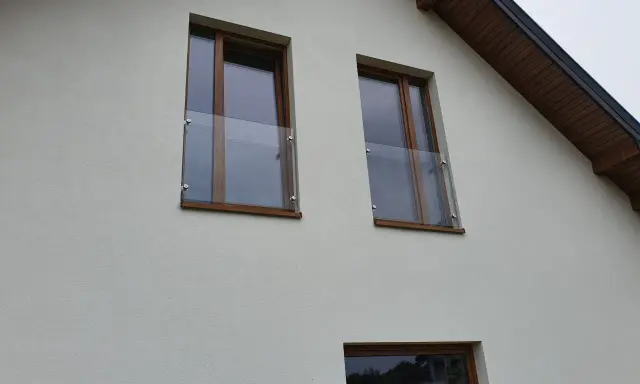 Nowoczesny portfenetr z drewnianymi ramami i szklaną balustradą na białej elewacji.