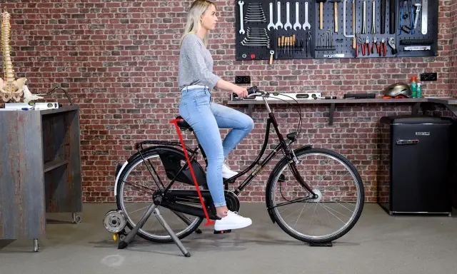 Frau sitzt auf einem Fahrrad auf einem Rollentrainer. Ein roter Pfeil zeigt die richtige Höhe des Fahrradsattels an, um den Fahrradsattel richtig einzustellen.