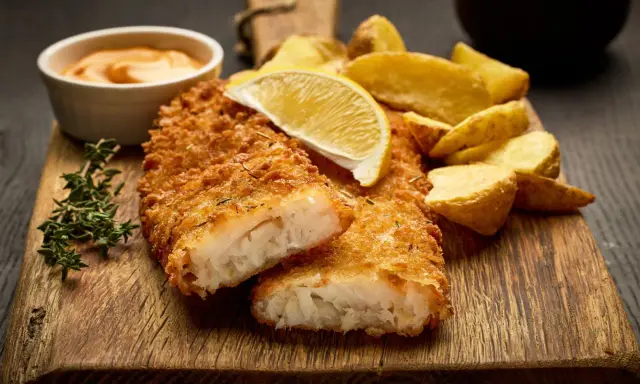 Krispigt panerad fisk, perfekt stekt, serveras med klyftpotatis och en citronskiva. En härlig måltid att njuta av.