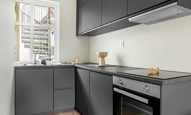 Diseño cocina restaurante moderno con gabinetes grises, encimera oscura y ventana con escalera exterior.
