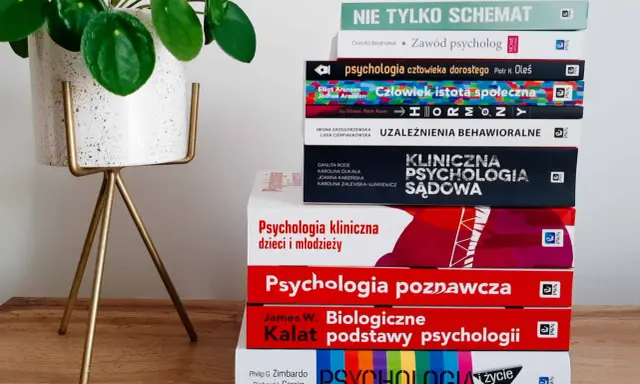 Książki o psychologii, w tym "Biologiczne podstawy psychologii" Kalata, na drewnianym tle obok rośliny.