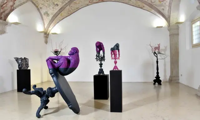 Sculture di scimmie e cervi colorati, opere di **artisti contemporanei famosi**, in una galleria con affreschi sul soffitto.