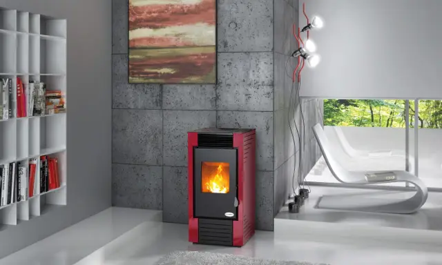 Estufa de leña o pellets roja con fuego encendido, junto a una estantería blanca y un sillón curvo.