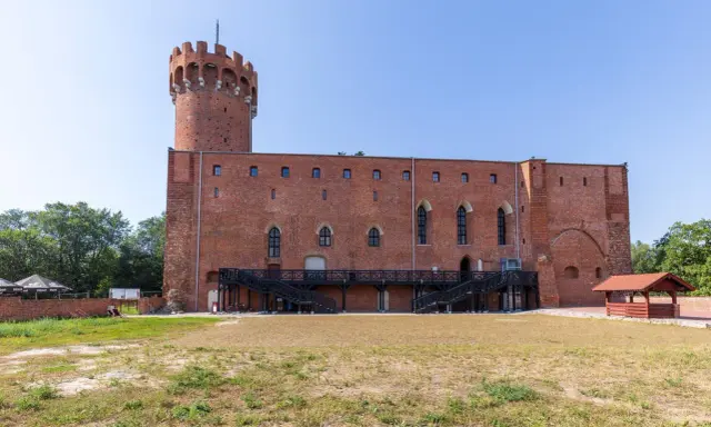 Zamek w Świeciu, ceglana twierdza z wieżą, otoczona zielenią i dziedzińcem.