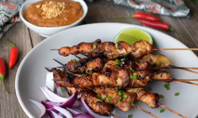 Pyszne satay z kurczaka na patyczkach, podane z sosem orzechowym, limonką i papryczkami chili.