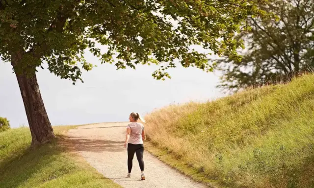 En kvinna går på en grusväg under ett träd. Hur lång tid tar det att gå en mil? Kanske en timme i detta vackra landskap.