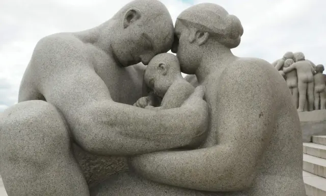 Kamienna rodzina w parku w Oslo, czułe objęcia rodziców otulających dziecko.