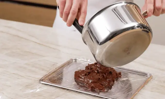 Comment faire fondre du chocolat : une casserole verse du chocolat fondu sur une plaque recouverte de film plastique.