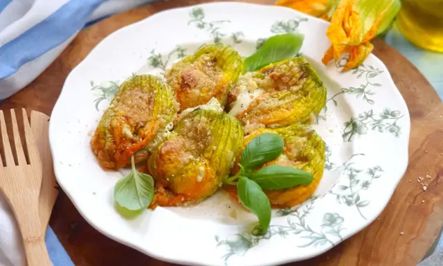 Deliziosi fiori di zucca al forno, ripieni e dorati, guarniti con basilico fresco su un piatto decorato.