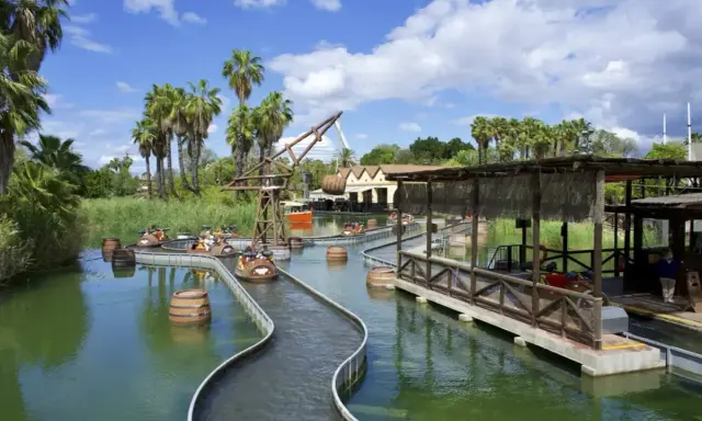 Atracción acuática con barcas y barriles flotantes, ideal para saber donde ir de vacaciones con niños. Palmeras y cielo azul.