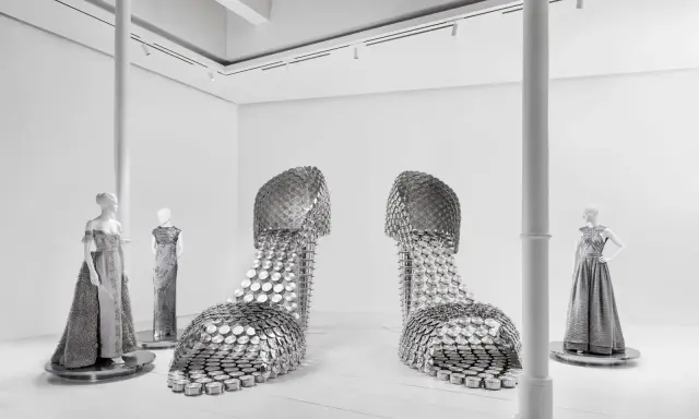 Installazione artistica mostra valentino roma: due enormi scarpe metalliche e abiti da sera su manichini.