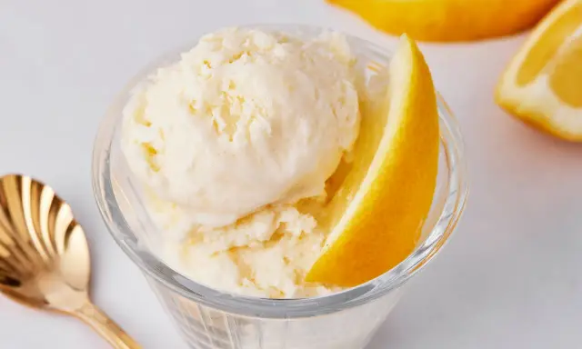 Erfrischendes zitroneneis selber machen: cremiges Eis in einer Glasschale, garniert mit Zitronenspalten und einer goldenen Löffel.