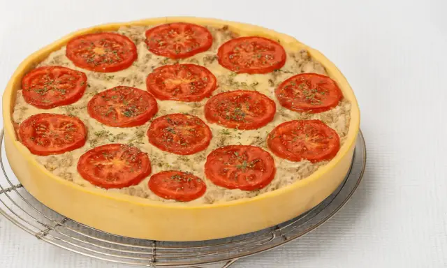 Une délicieuse quiche au thon, garnie de rondelles de tomates fraîches et d'herbes, prête à être dégustée.