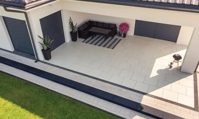 Nowoczesny taras z jasnej kostki brukowej, z wygodnym narożnikiem i grillem.