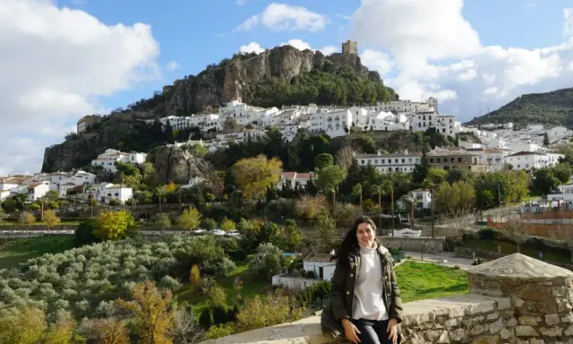 Una mujer sonríe ante el pintoresco pueblo blanco de la sierra de Cádiz, coronado por un castillo.