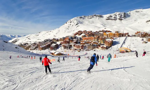 Ośrodek narciarski we francuskich Alpach. Tłumy narciarzy i snowboardzistów na stoku, w tle zabudowania. Francja narty gdzie najlepiej? Tutaj!