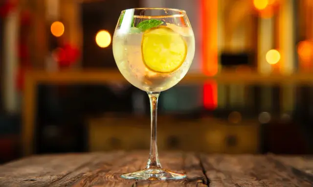 Erfrischender Martini Bianco Spritz mit Zitrone und Minze auf einem Holztisch, im Hintergrund unscharfe Lichter.