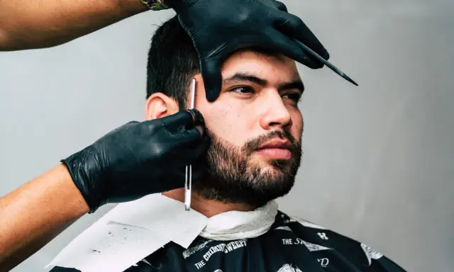Barber precyzyjnie goli zarost brody ostrym narzędziem.