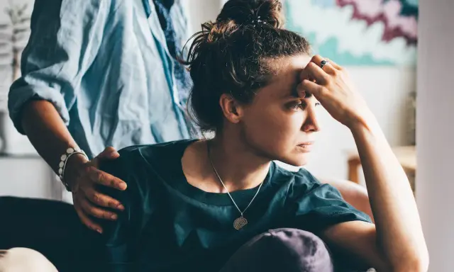 Una donna pensierosa, con una mano sulla fronte, riceve un gesto di conforto. Potrebbe riflettere sull'attaccamento evitante e la sessualità.