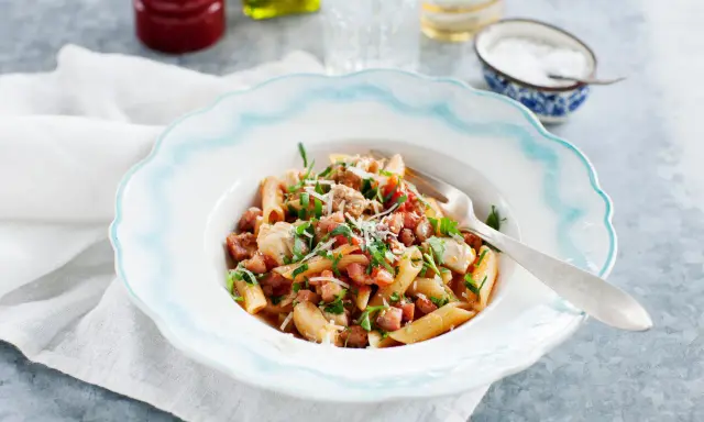 En tallrik med penne pasta, kyckling och tärnad pancetta, toppad med persilja och parmesan. Ett enkelt pancetta recept för en god middag.