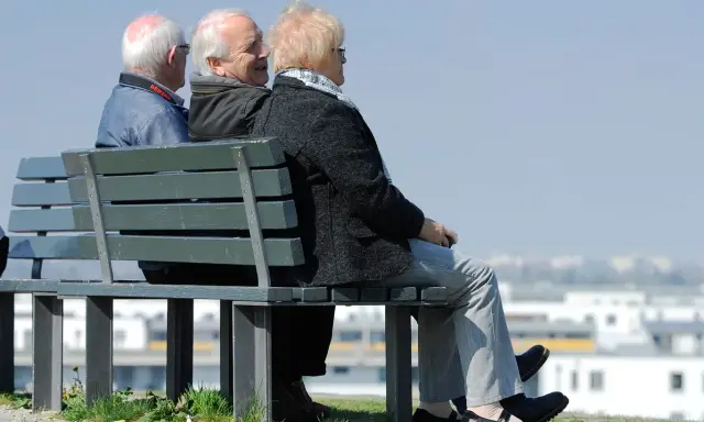 Trzech seniorów siedzi na ławce, rozmawiając. Może to dyskusja o tym, czym jest emerytura pomostowa i jakie daje możliwości.