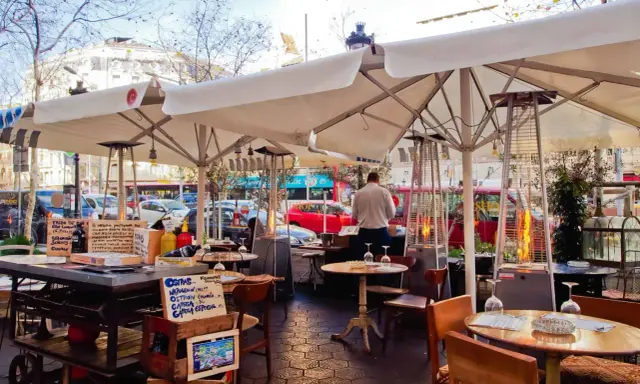 Terrasse d'un restaurant à Barcelone, avec des tables, des parasols, des chauffages d'extérieur et des panneaux indiquant des plats typiques espagnols.