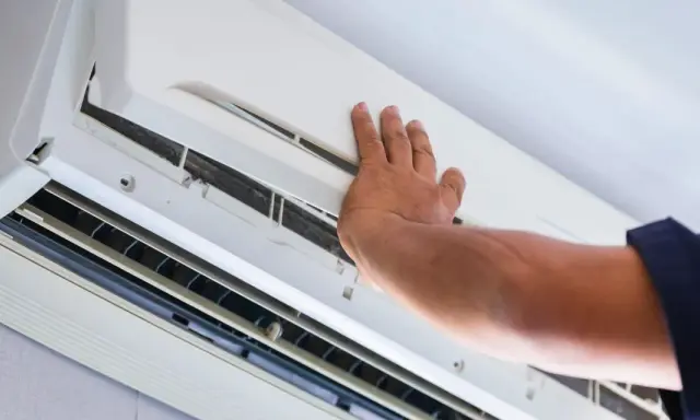 Main d'un technicien ouvrant un climatiseur pour vérifier l'eau et le filtre.