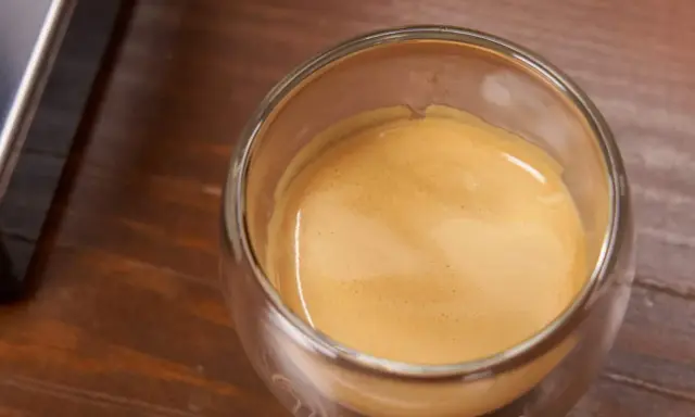 Ein Glas Espresso mit einer feinen Crema auf einem Holztisch. Ein kleiner Schuss Sahne macht den Kaffee mit Sahne gesund und lecker.