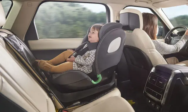 Bebé sonriente en silla de coche a contramarcha, viajando segura mientras mamá conduce.