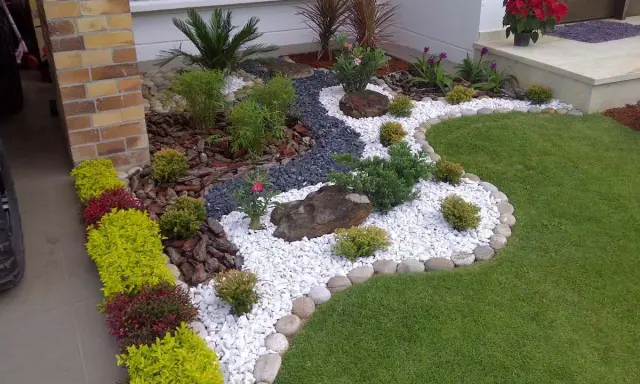 Un jardin moderne avec des graviers blancs, des plantes vertes et des roches. Une belle idee jardin deco pour un extérieur soigné.