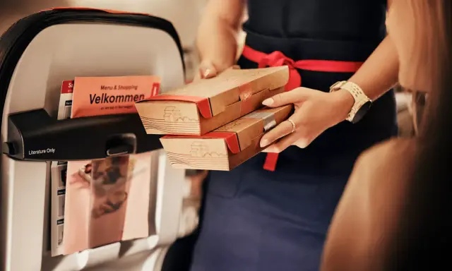 Serverar mat ombord, kanske en del av norwegian taxfree ombord-utbudet. En "Velkommen"-folder syns i fickan.
