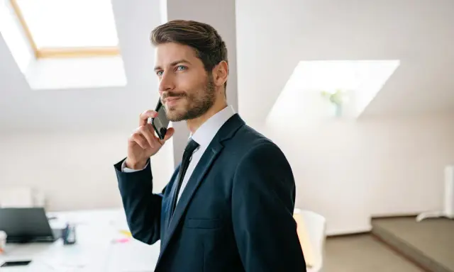 Mężczyzna w garniturze rozmawia przez telefon, jego wyraz twarzy sugeruje, że nastąpiła **zmiana głosu podczas rozmowy**.